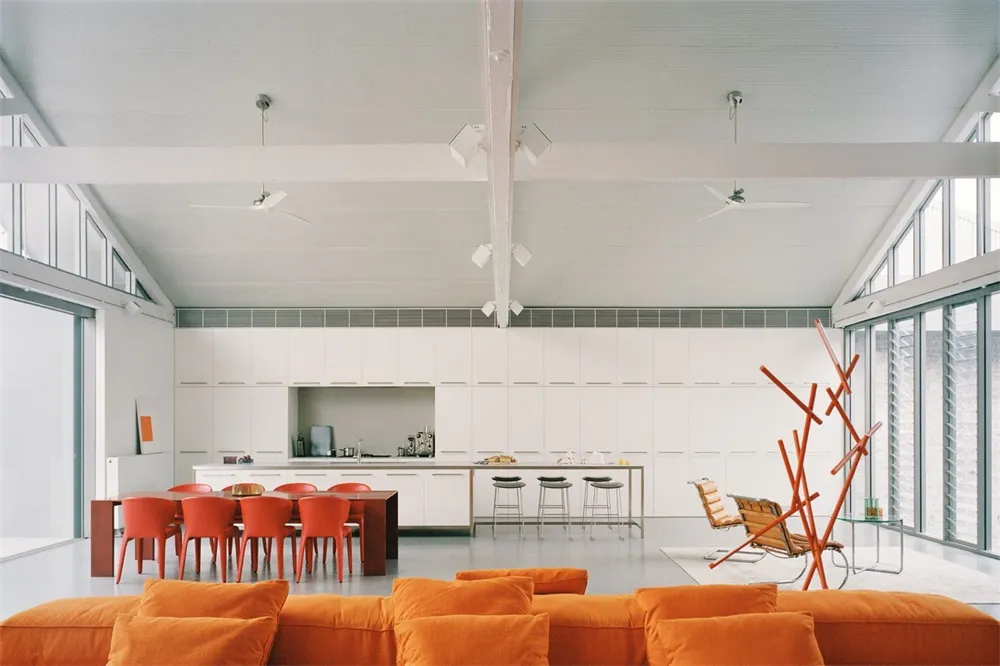 A minimalist living room with an orange sofa, white cabinets, and modern furniture.