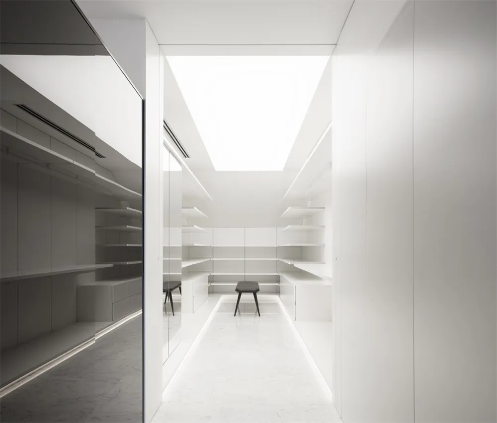 A minimalist white closet with clear glass sliding doors and shelves.