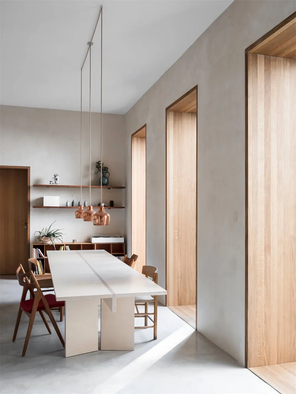 Modern dining room with concrete table, wooden chairs, and metal pendant lights hanging from the ceiling.