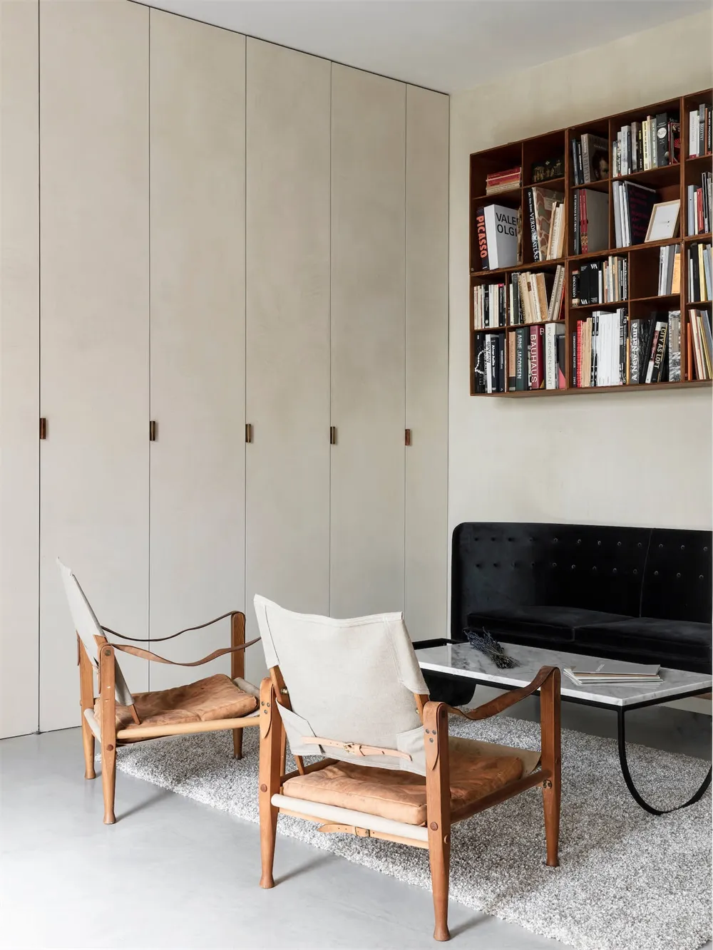 A modern living room with wooden chairs and a black sofa, featuring a bookshelf filled with books.