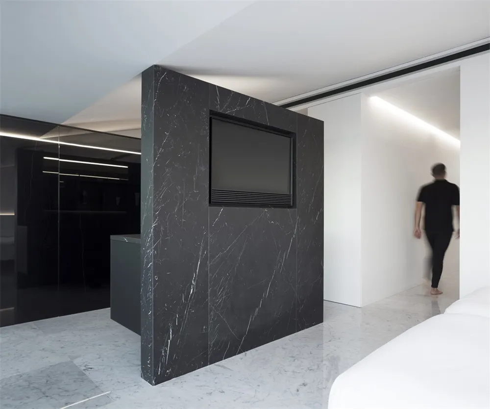 A modern kitchen with a black marble backsplash and black marble countertops, featuring a black television mounted on the wal