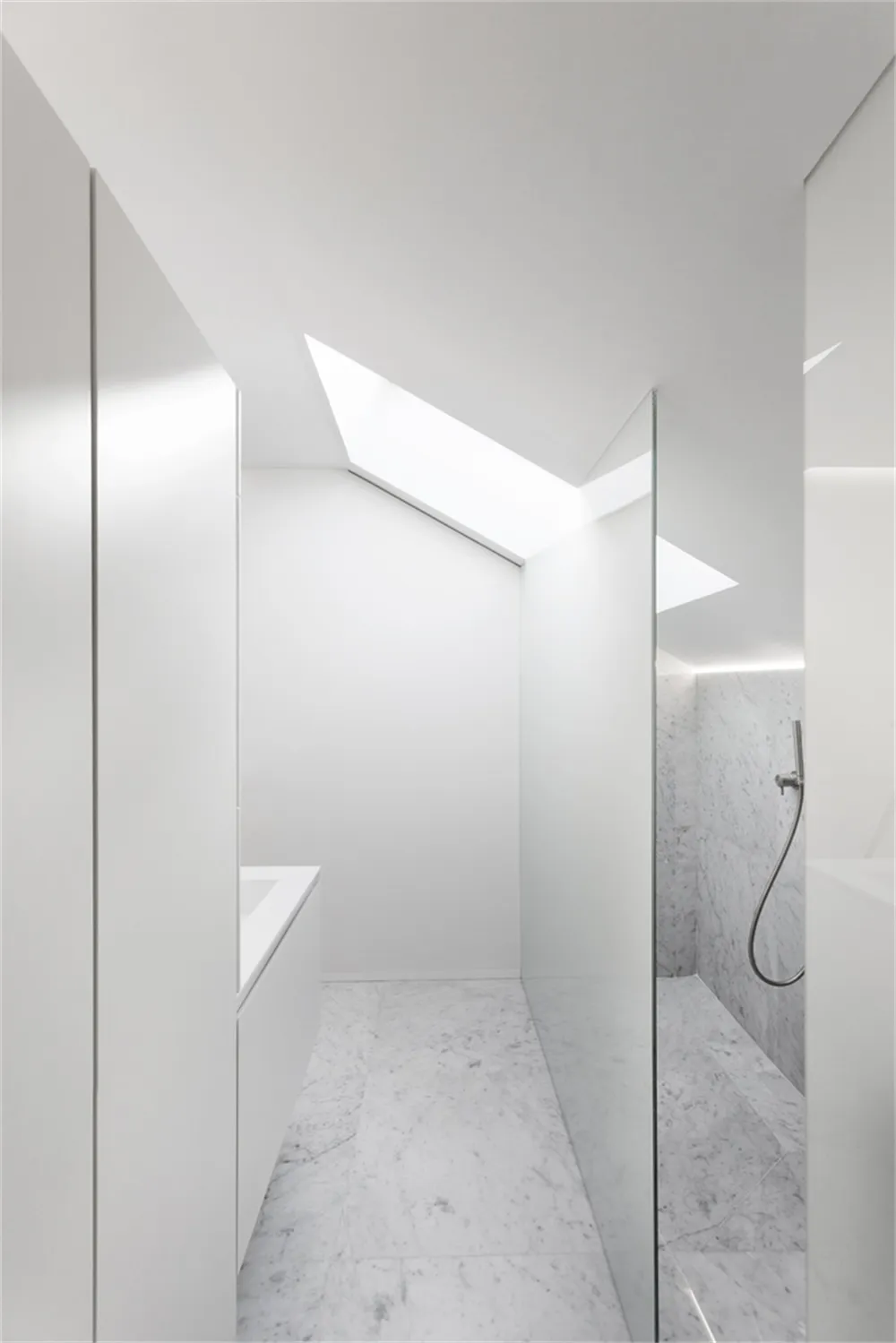 A minimalist bathroom with marble walls and floor, featuring a skylight and white fixtures.