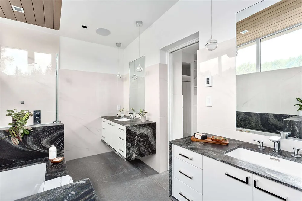A modern bathroom with sleek marble countertops and flooring, featuring a minimalist design with white cabinetry and pendant