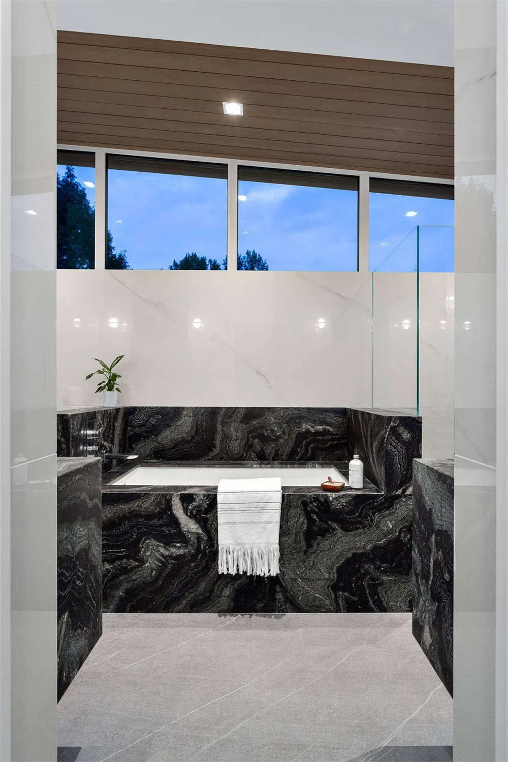 Modern bathroom featuring black marble with a white towel hanging on the edge of the bathtub and a plant on the left side.