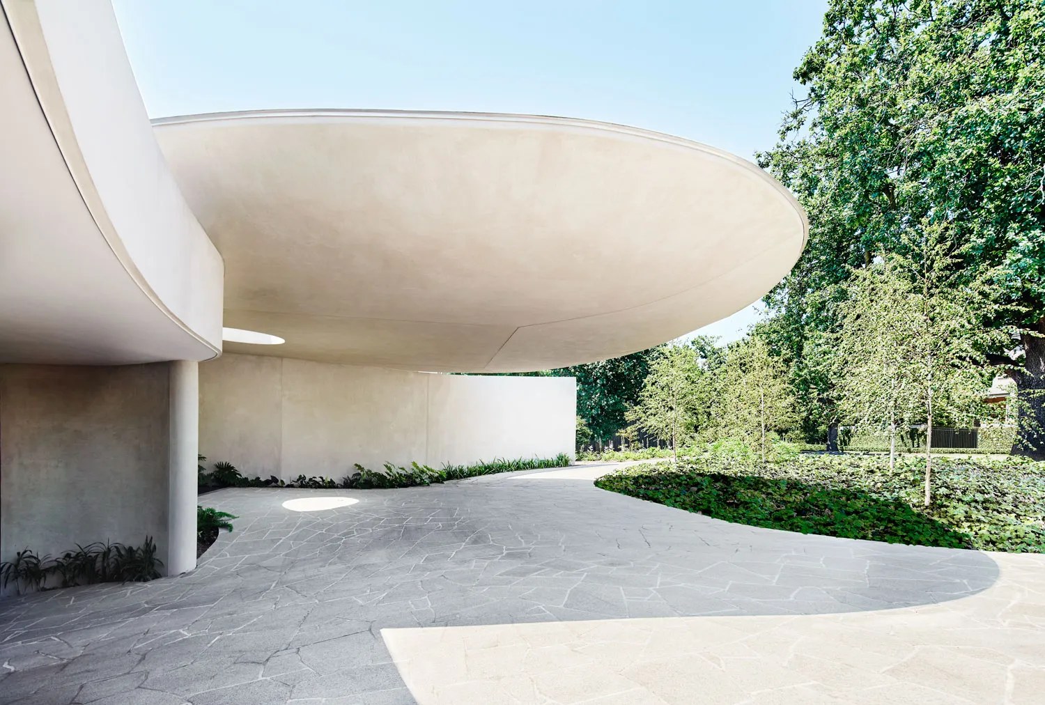 Modern architectural design featuring a sleek, concrete exterior with curved walls and a large, overhanging canopy.