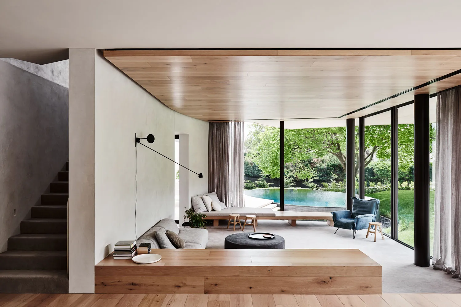 Modern residential living room with a pool view, featuring wood and concrete materials, and a comfortable seating area.