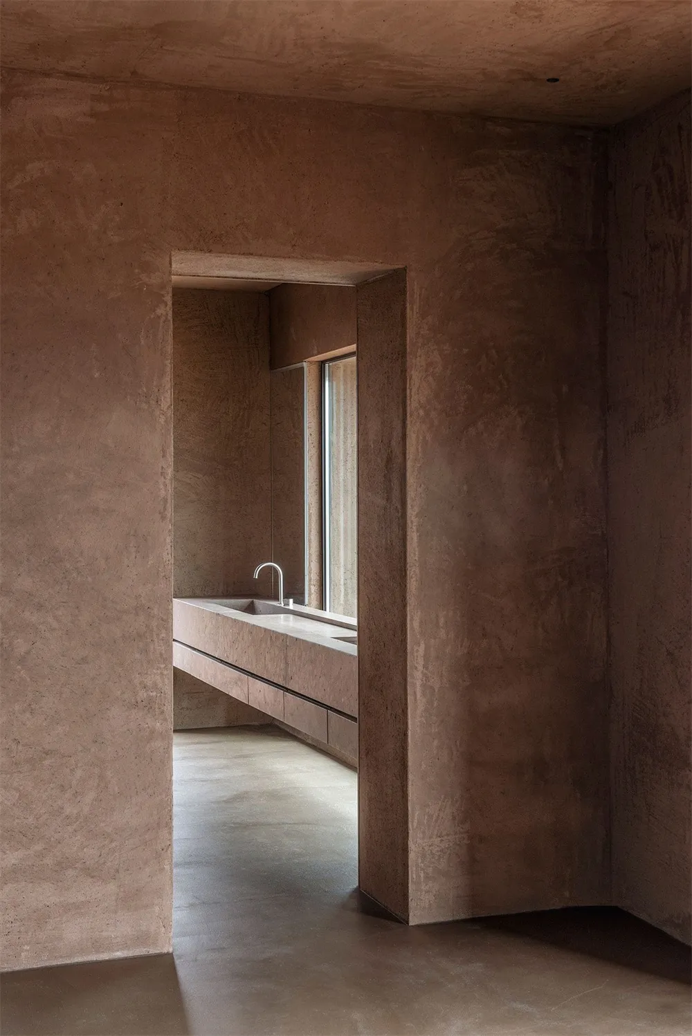 Modern bathroom with concrete walls and floor, featuring a minimalist sink and natural light from a large window.