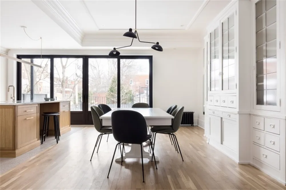 Modern minimalist dining room featuring a sleek white table surrounded by black chairs, set against a backdrop of tall window