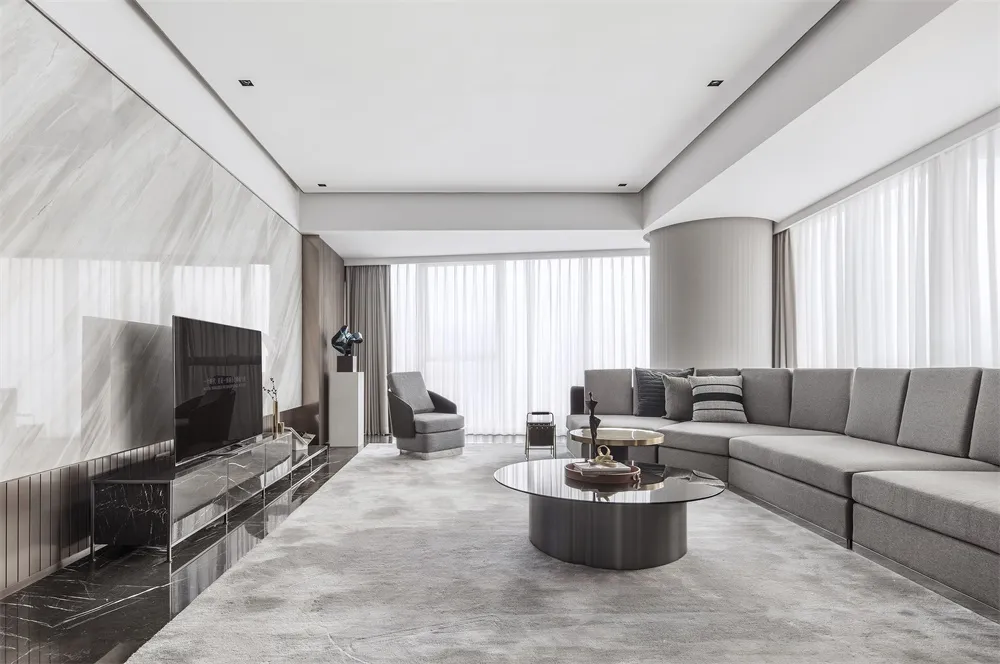 A modern minimalist living room featuring a gray sectional sofa, a round glass coffee table with marble accents, and a marble