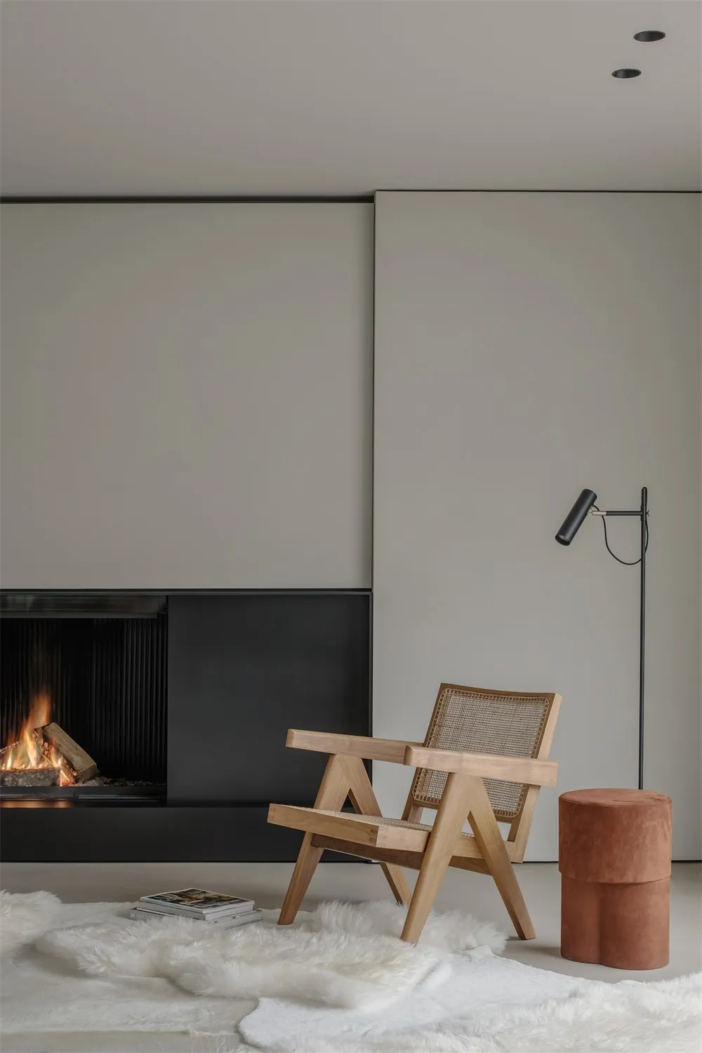 A minimalist interior design featuring a wooden armchair on a fur rug, a fireplace, and a modern floor lamp in a living room.
