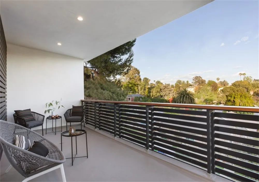 A modern balcony featuring a wooden and metal railing with a view of trees and sky.