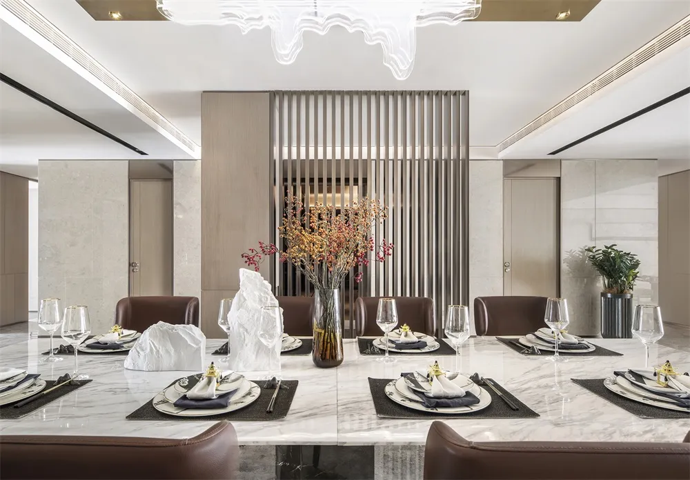 Modern dining room featuring marble table and chairs, with a centerpiece of dried flowers in a vase and place settings on the