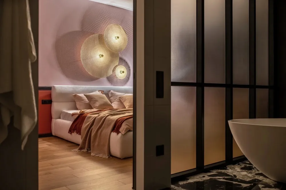A modern bedroom featuring textured wall lights, a cozy bed, and a clean, minimalistic design.