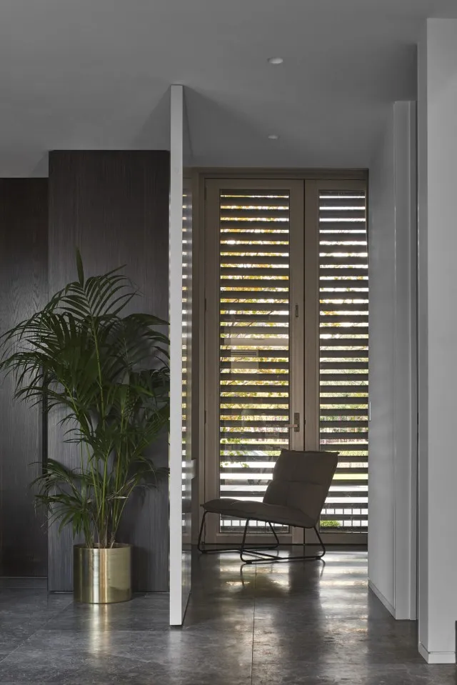 A hallway with a modern interior design featuring a metal floor, large planter with a plant, and a metal chair with a black c