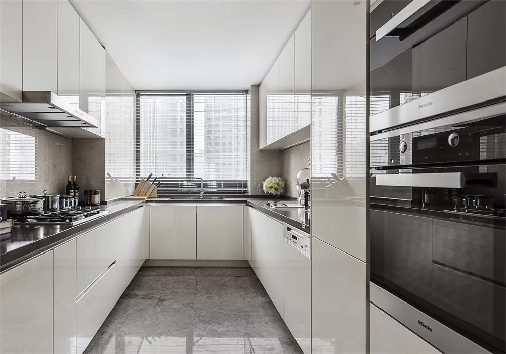 Modern kitchen with white cabinets, stainless steel appliances, and a window with blinds.