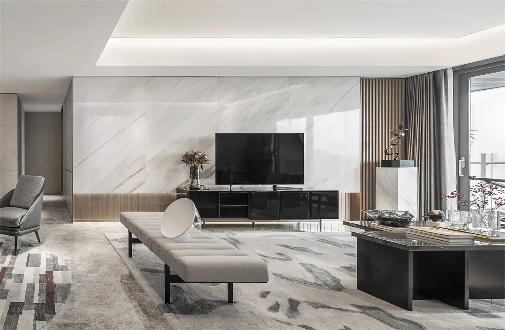 A modern living room with a marble accent wall, black furniture, and a light-colored bench in front of a television.