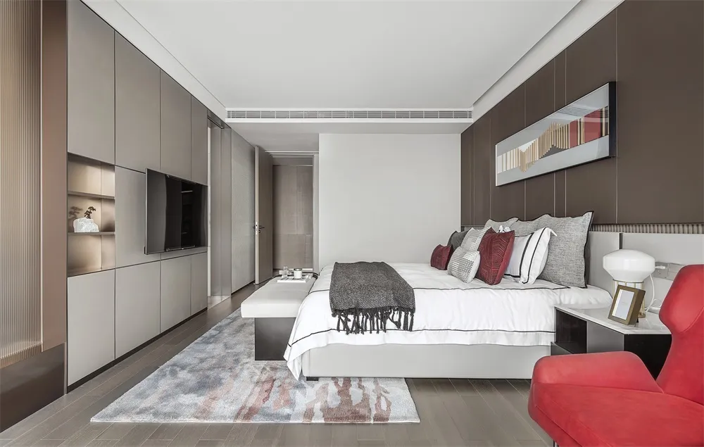 Modern minimalist bedroom with white bed, grey and red pillows, and a red accent chair, featuring gray and pink rug, white an