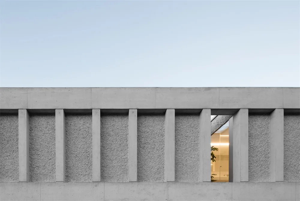A modern building exterior with concrete pillars and a view into a well-lit interior space.