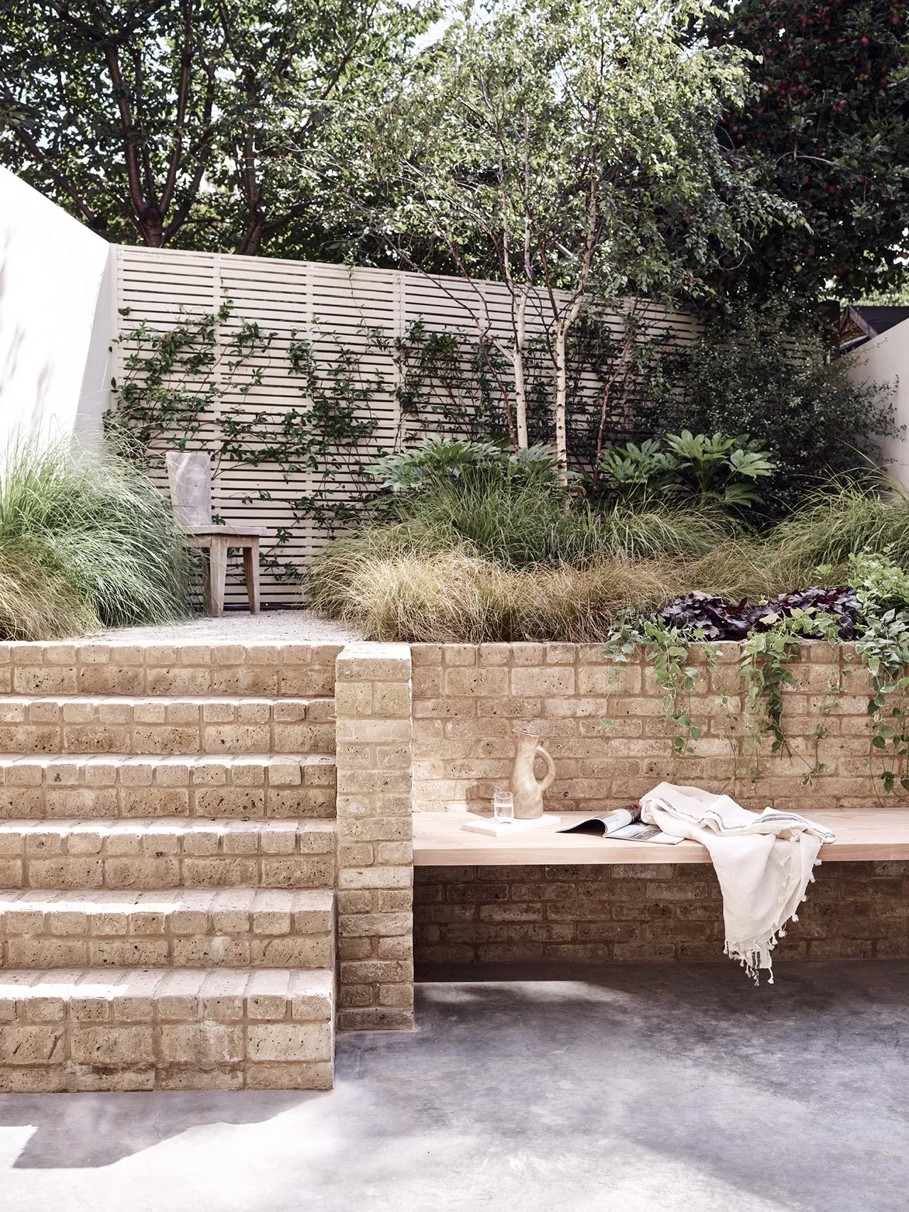 A modern garden featuring brick stairs, wooden bench, concrete patio, and fabric draped over furniture.