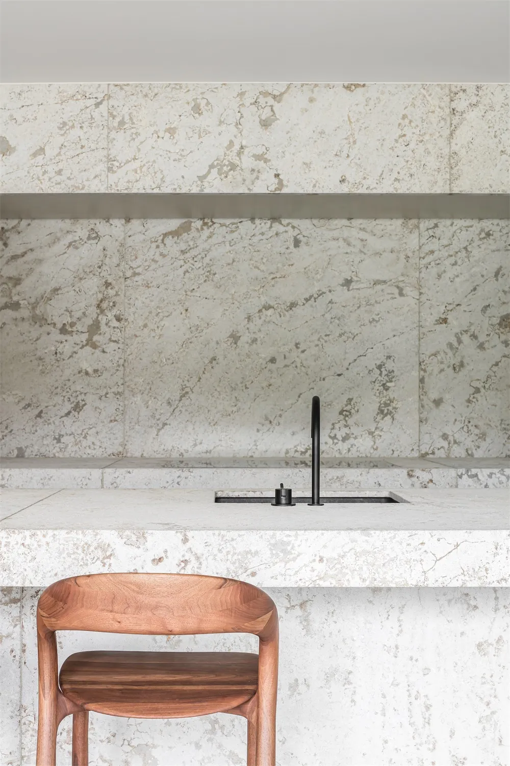 A modern kitchen featuring white marble countertops and a wooden chair.