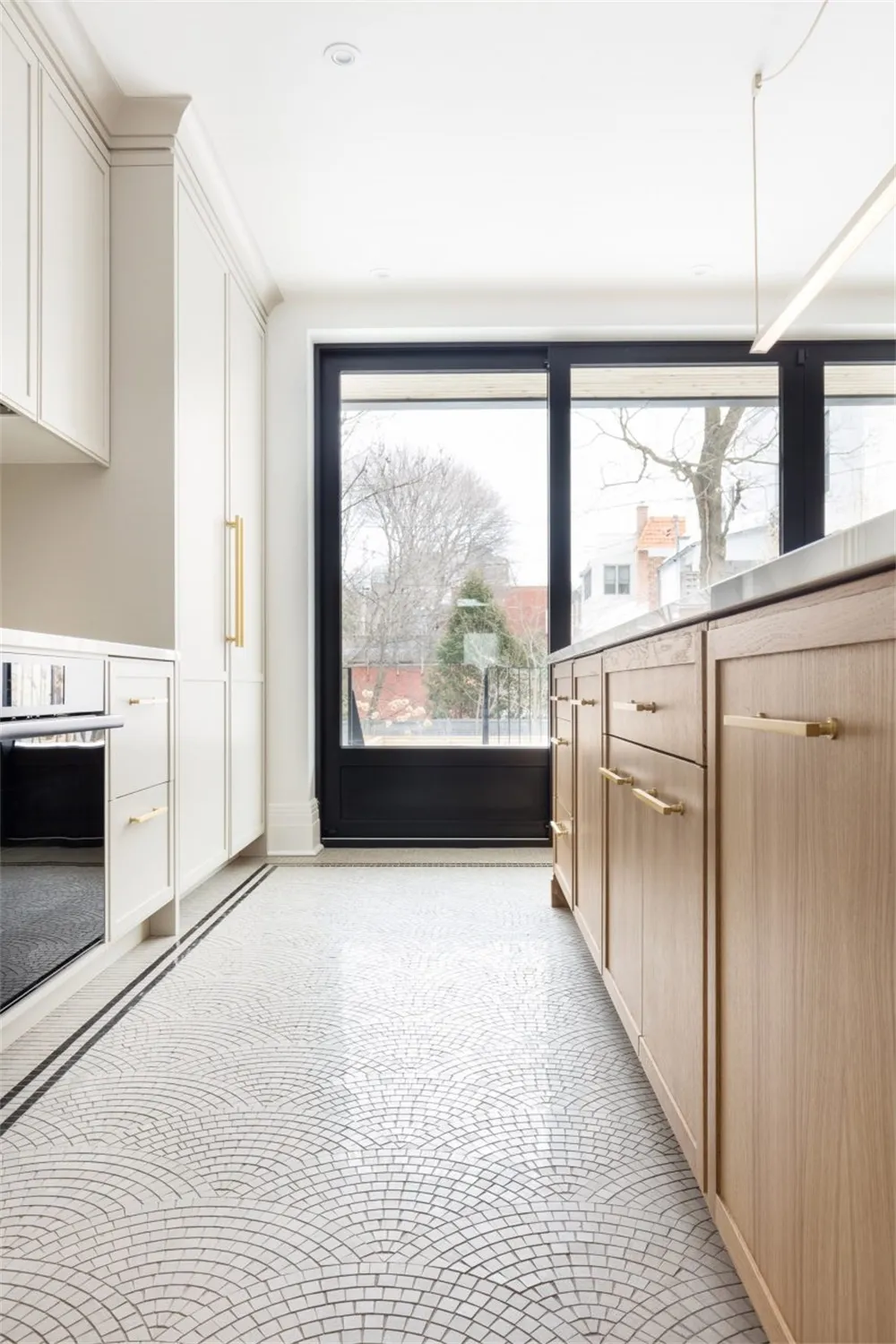 A modern kitchen featuring a tile floor with a wave pattern, wooden cabinets with brass handles, and large windows with a vie