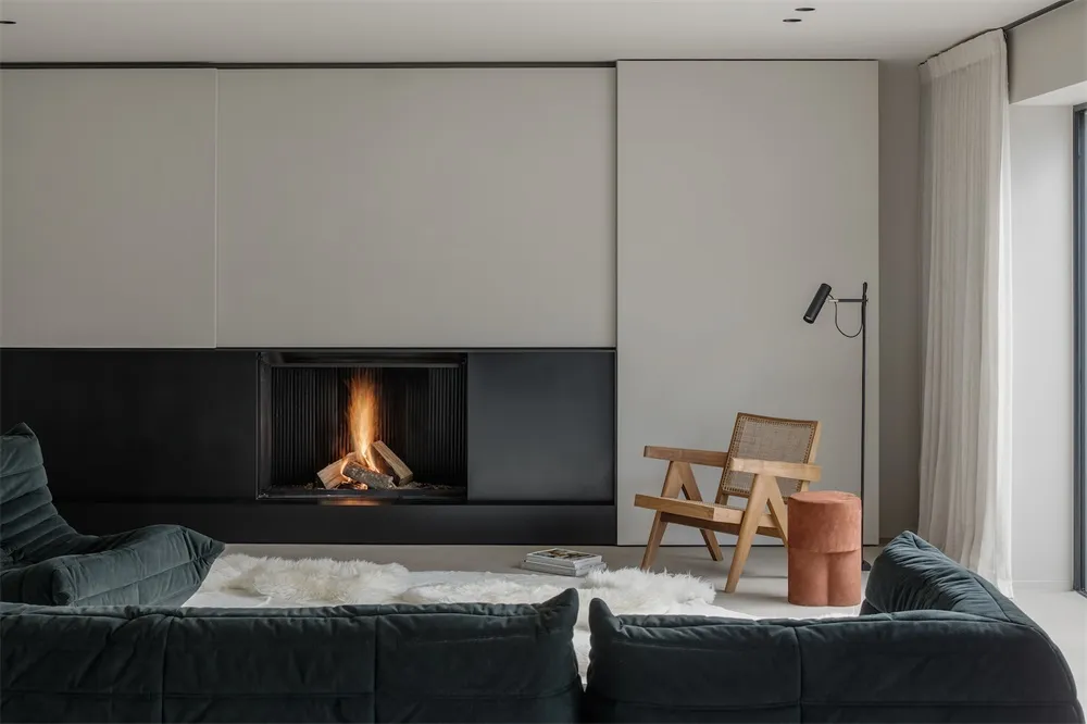 Modern living room with a metal fireplace, fabric seating, and wooden chair.