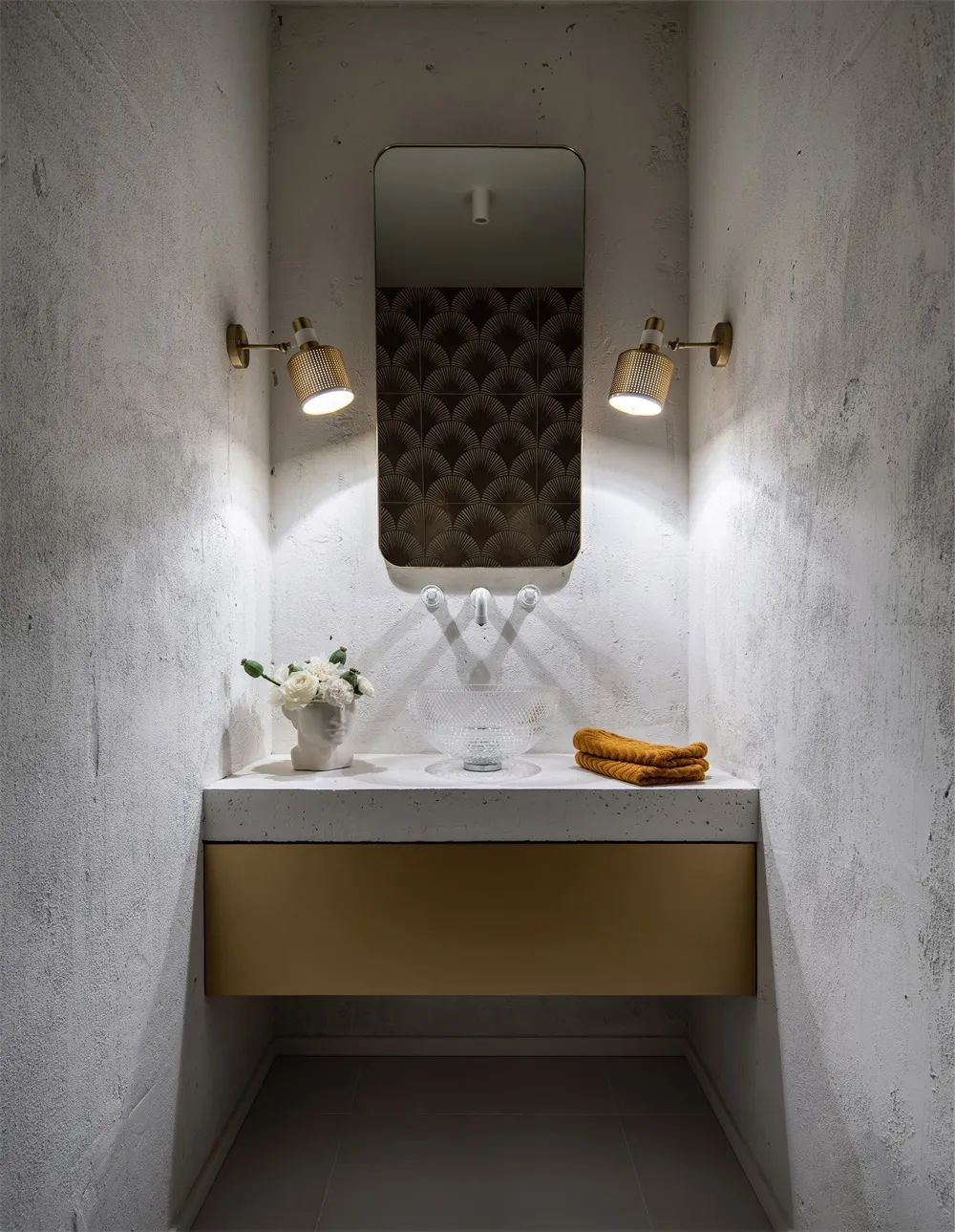 Minimalist bathroom with concrete walls and a modern sink. White flowers and golden accents.
