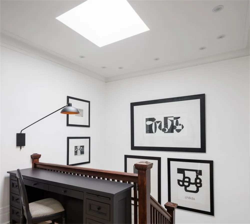 A modern home office featuring a black desk, white walls, and framed black and white photos on the wall.
