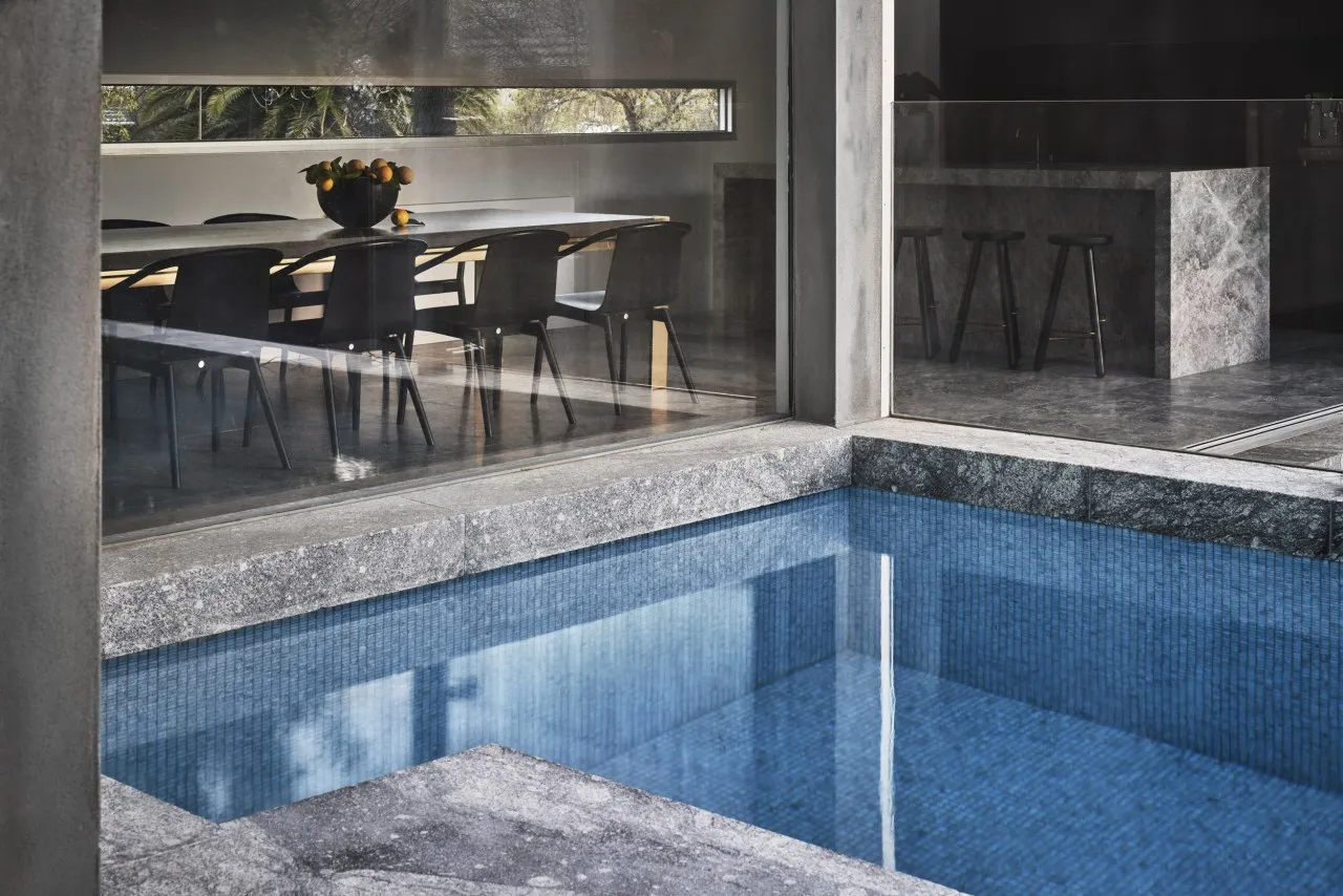 A modern indoor swimming pool with granite tiles, featuring a table with oranges in the background.