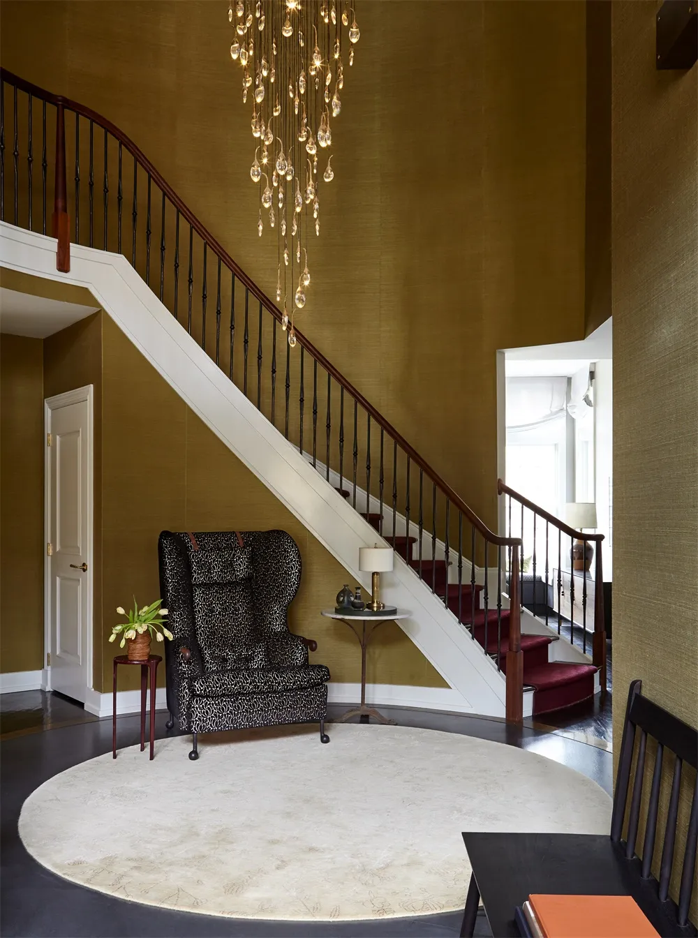 Modern staircase entry with hardwood floors, dark wood railings, and a hanging chandelier.