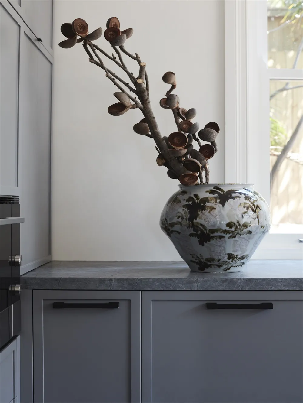 A minimalist ceramic vase containing dried plant branches on a sleek, modern kitchen countertop.