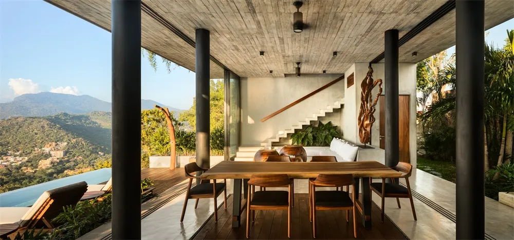 Modern minimalist living room with concrete walls, wooden floors, and a large window overlooking a scenic mountain view.