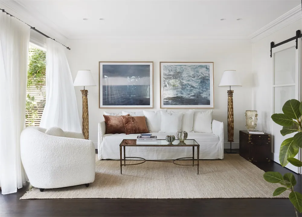 A minimalist living room with white furniture, a glass coffee table, and metal floor lamps.