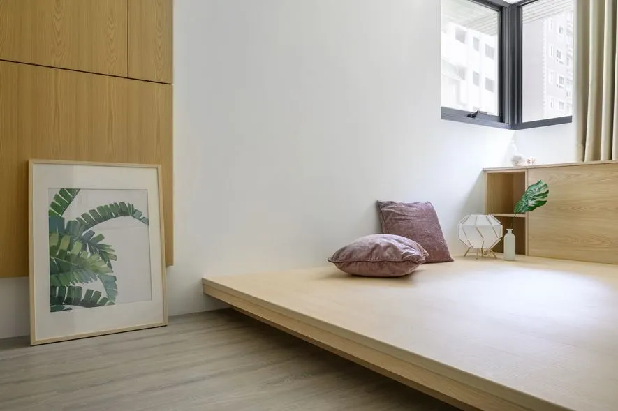 Modern minimalist bedroom featuring a floating bed platform with pink pillows and a framed botanical print hanging on the wal