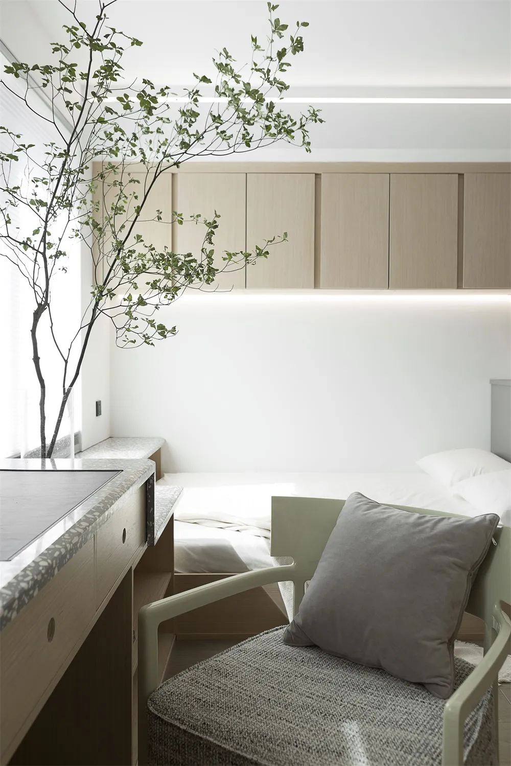 A minimalist bedroom featuring a fabric chair with a cushion, modern furniture, and a green plant.