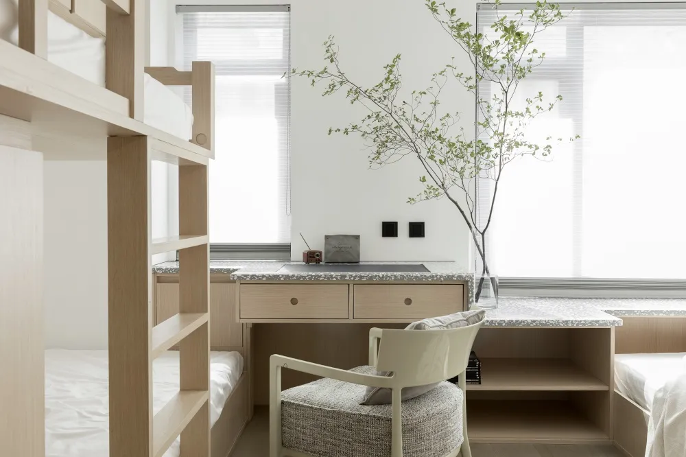 A minimalist modern bedroom interior featuring a wooden bunk bed and a stone-topped desk with a plant on it.