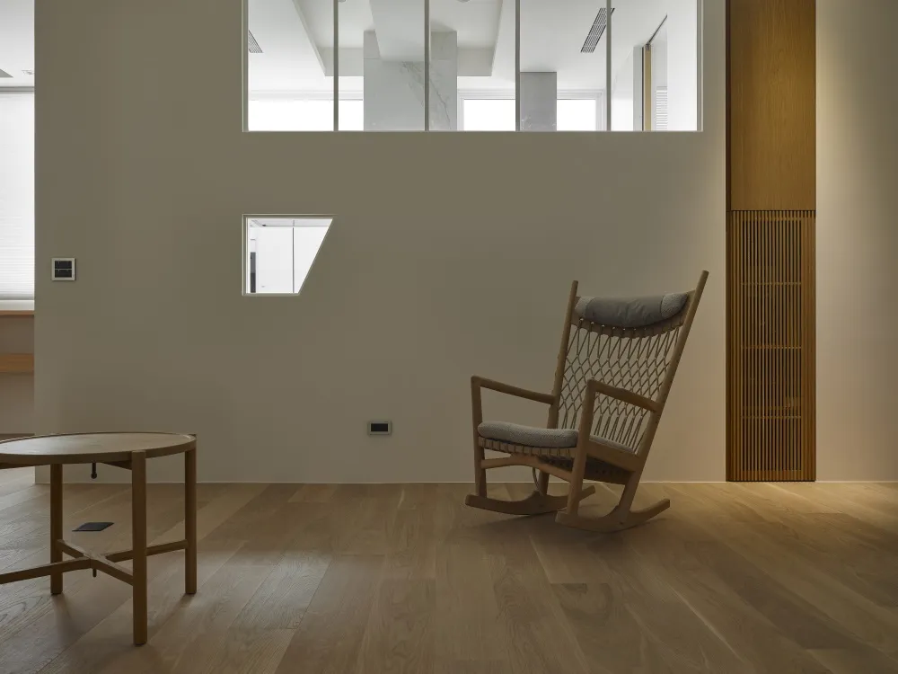 A minimalist home interior featuring a wooden floor, a rocking chair, a wooden coffee table, and a wooden column.