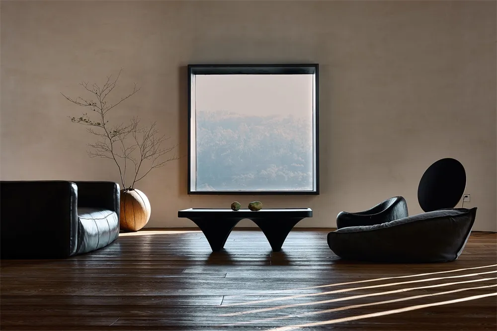 A minimalist living space featuring wooden furniture, a large window with a view of a forest, and a black coffee table with t