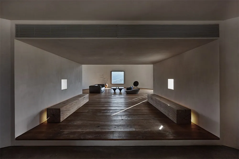 Modern living room featuring minimalist wooden furniture and concrete floor and walls with a large window.