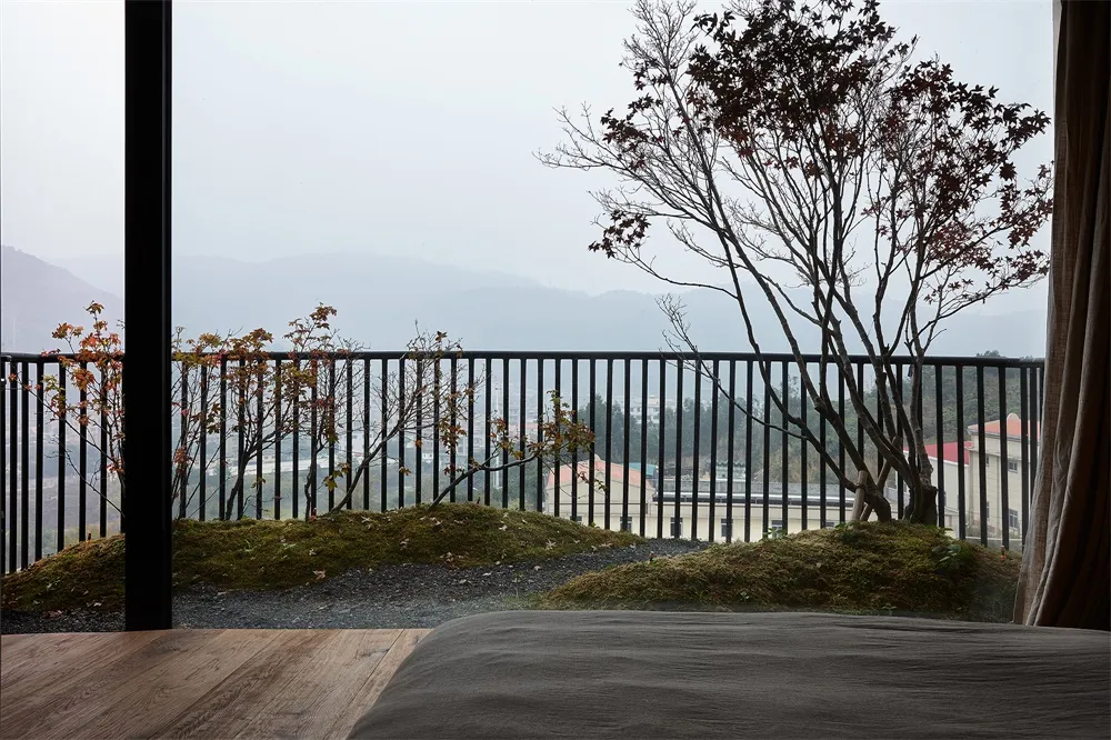 A bedroom with a view of a tree and mountains through a window