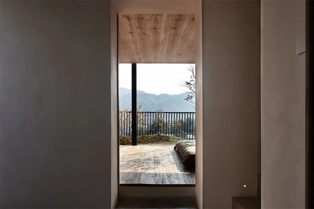 Minimalist balcony featuring wood flooring and railings, with a view of distant mountains and leafless trees.