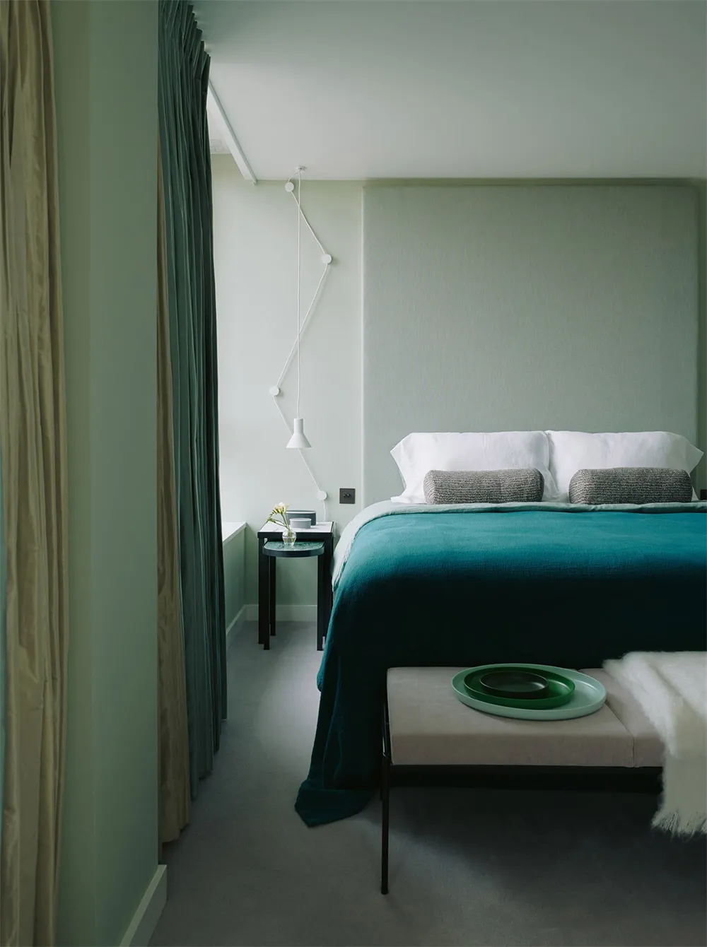 Modern minimalist bedroom featuring a bed with a teal bedspread, white pillows, and a metal bed frame, with green curtains an