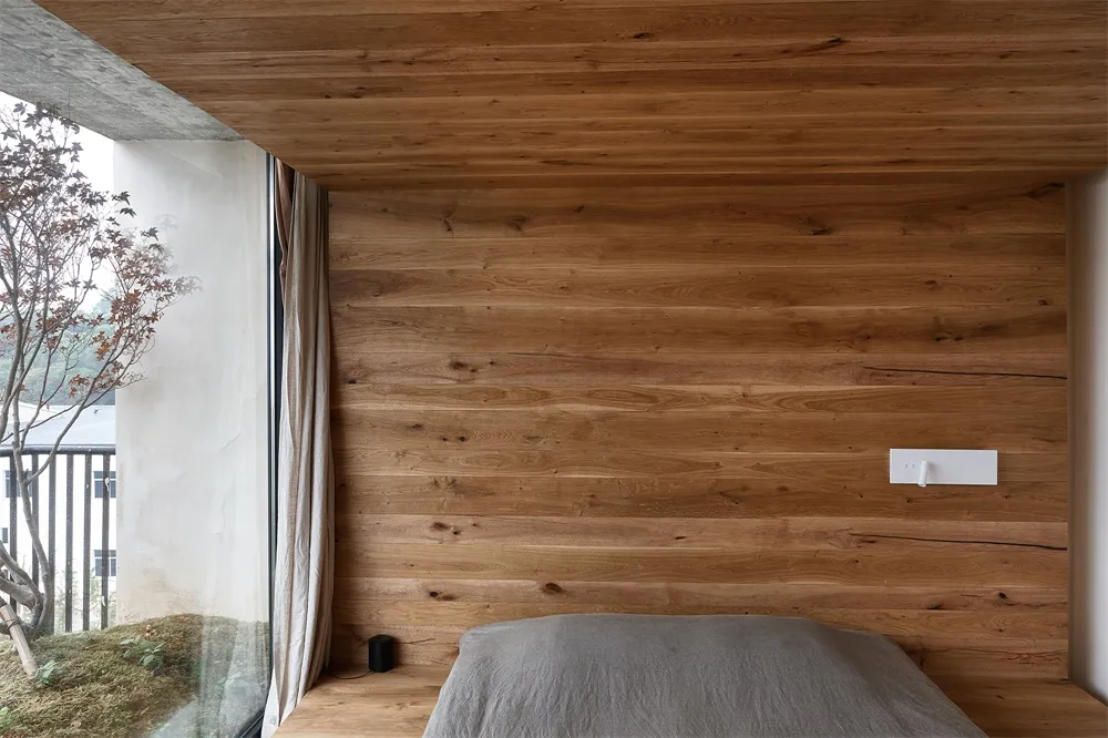A minimalist bedroom featuring wooden walls and a bed with a grey sheet.