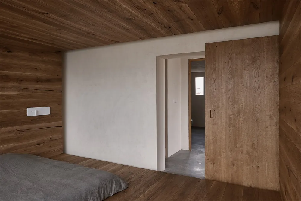 A minimalist bedroom featuring wood-paneled walls and a carpeted floor.