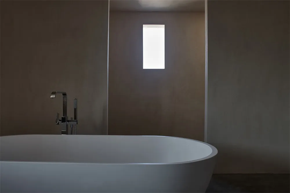 A modern bathroom with concrete walls, a freestanding bathtub, and a rectangular window.