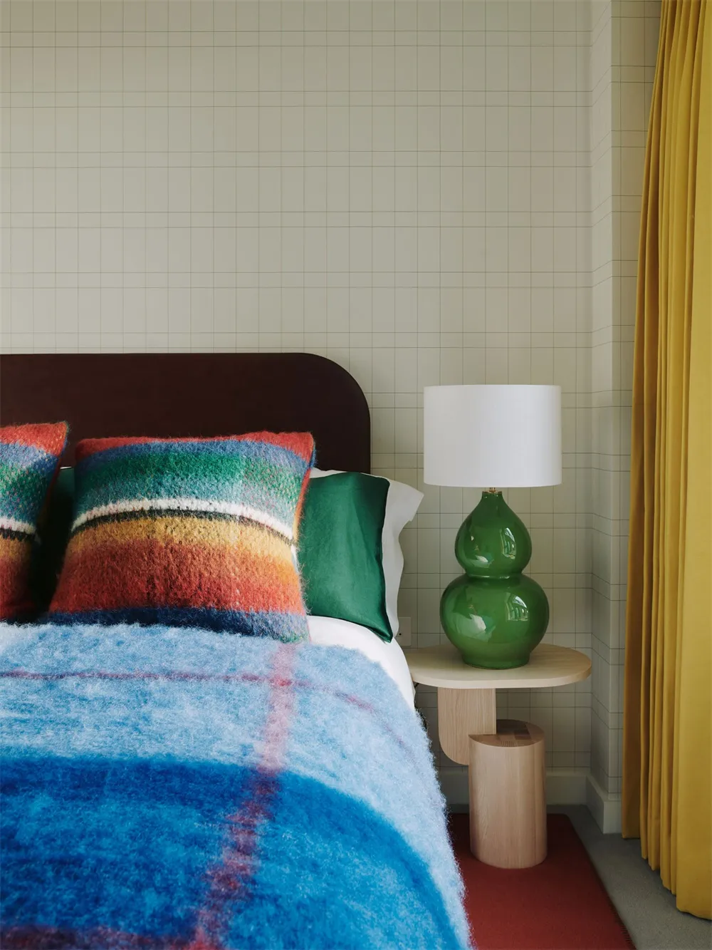 A modern bedroom featuring colorful textiles and a green lamp on a side table.
