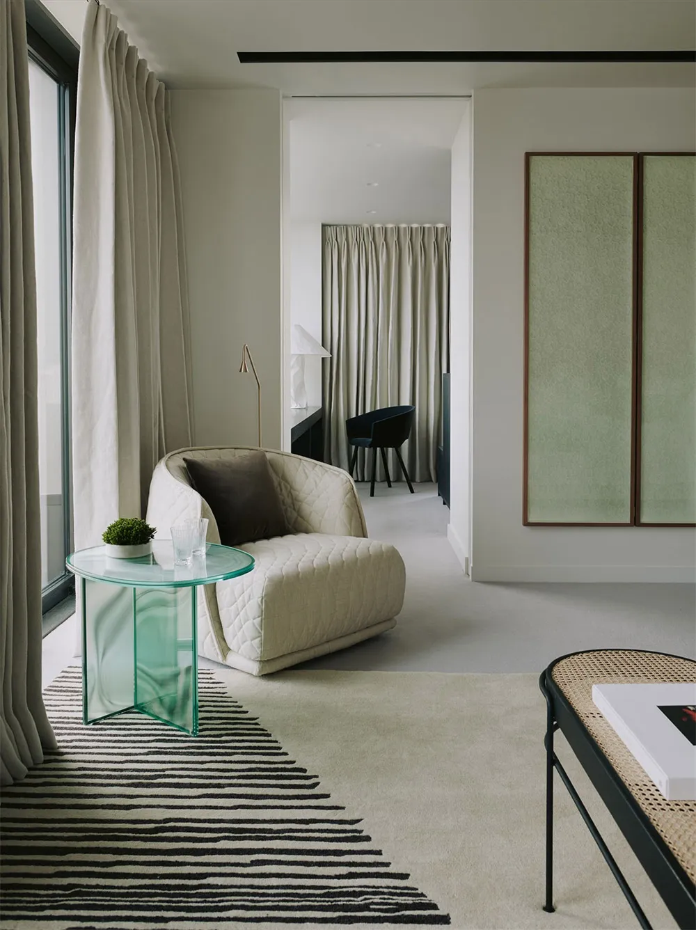 A modern minimalist living room featuring a fabric couch, a glass bedside table, and a striped rug.