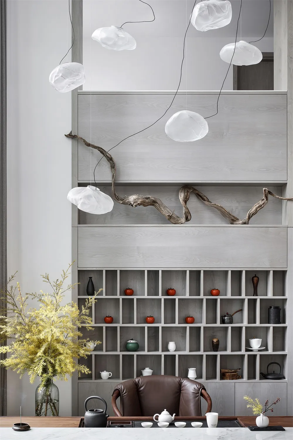 Modern minimalist living room featuring a tea set on a wooden shelf, with a natural plant in the foreground and cloud-shaped 