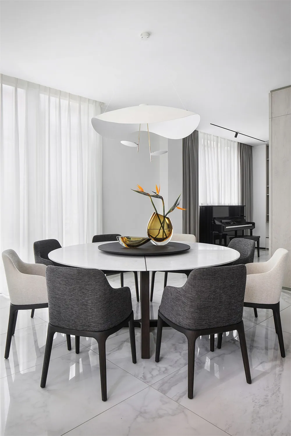 Modern dining room with a round marble table, fabric chairs, and metal accents.