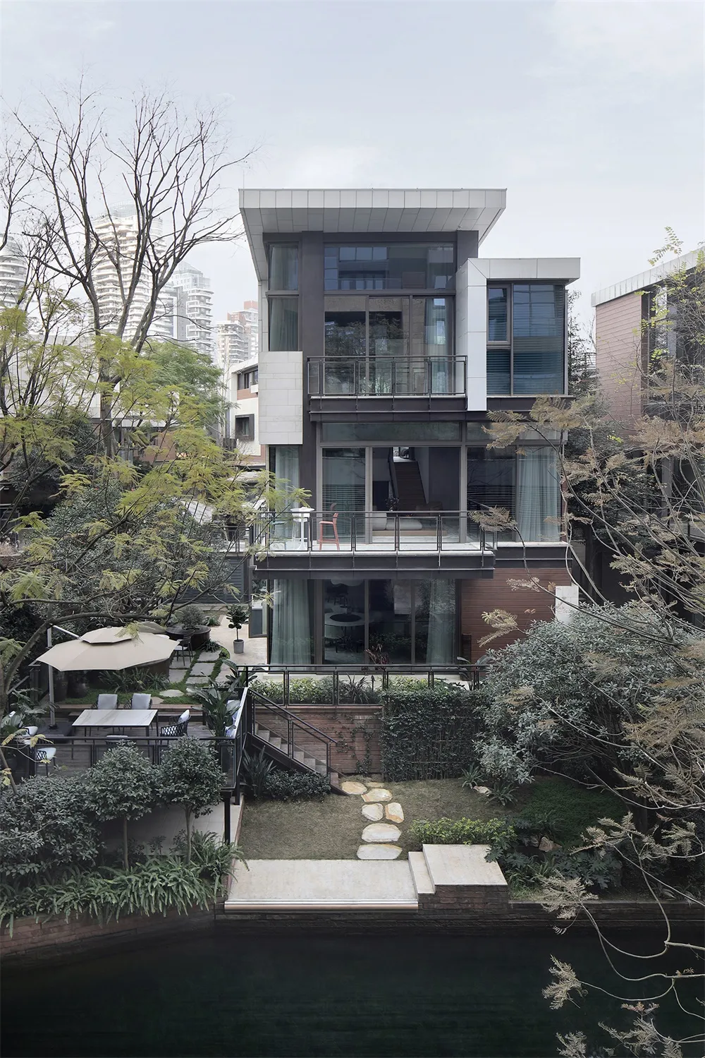 一座擁有玻璃立面的現代住宅,石板步道通往入口,周圍環繞綠意與樹木。